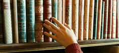 a person's hand reaching for a book on a bookshelf