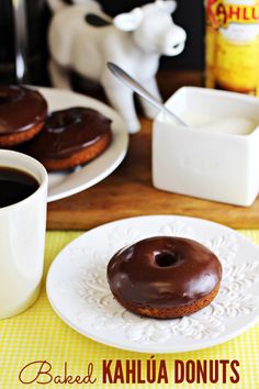 a chocolate donut sitting on top of a white plate next to a cup of coffee