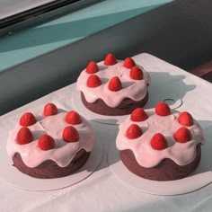 three cakes with strawberries on top are sitting on a white tablecloth near a window