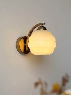 a wall light that is on the side of a wall with flowers in front of it