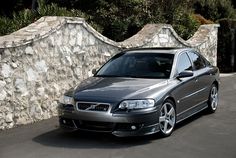 a silver car parked in front of a stone wall