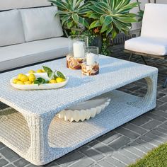 a wicker coffee table with lemons and candles on it in front of a white couch