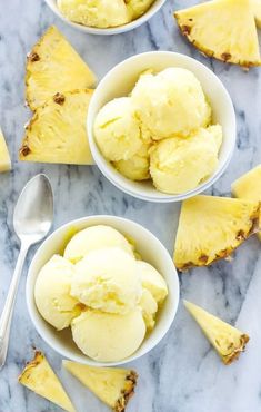 three bowls filled with ice cream next to slices of pineapple on a marble surface