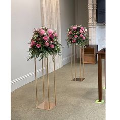 two tall gold vases with pink flowers in them on the floor next to each other