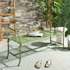 a green metal table sitting on top of a rug next to a plant and books