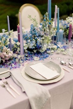 the table is set with blue and white flowers, silverware, and napkins