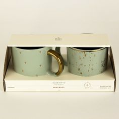 two coffee mugs are in a box with gold rings on the inside and outside