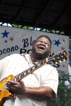 a man playing an electric guitar in front of a sign that says coconut blues festival