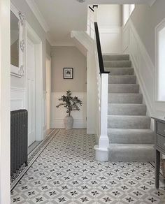 a white and gray hallway with stairs, potted plant and pictures on the wall