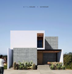 a person standing in front of a concrete building with cactuses on the ground and people walking by