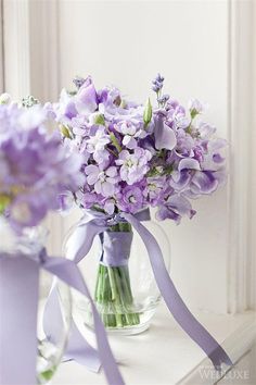 purple flowers are in a glass vase on a window sill next to a lavender ribbon