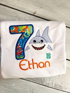 a white shirt with a shark and number seven on it's chest, sitting on a wooden surface