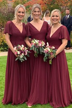 three bridesmaids in maroon dresses posing for the camera with their bouquets and flowers