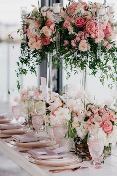 the table is set with pink and white flowers, greenery, candles and plates