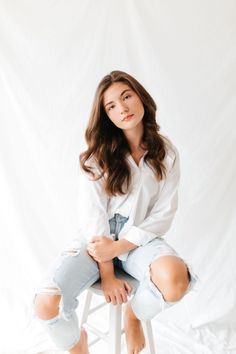 a woman sitting on top of a white chair with her legs crossed and looking at the camera