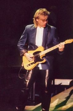 a man playing an electric guitar while wearing leather pants and a black blazer on stage