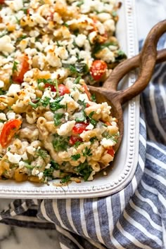 a casserole dish filled with pasta, vegetables and feta cheese on a striped towel