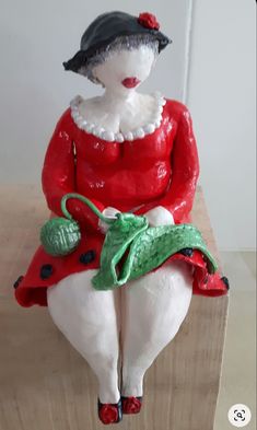 a ceramic figurine sitting on top of a wooden block wearing a red dress and black hat