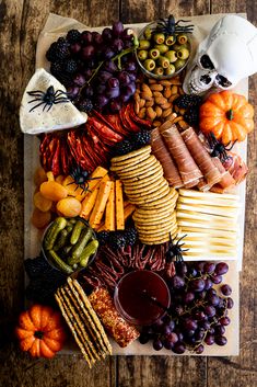 a platter filled with cheese, crackers, fruit and other foods on top of a wooden table