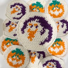 several crocheted coasters with orange, green and purple designs are arranged on a white surface