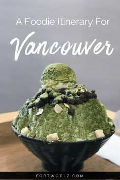 a black bowl filled with green food on top of a wooden table