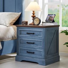 a night stand with two drawers and a clock on the top, next to a bed