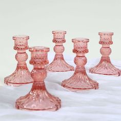 a group of pink glass candlesticks sitting on top of a white tablecloth