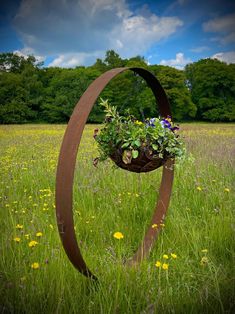 a metal sculpture in the middle of a field with flowers growing out of it's sides