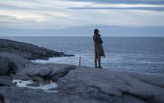 a woman standing on top of a rocky beach next to the ocean