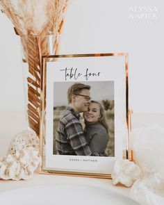 a photo frame with a couple on it next to some dried flowers and a vase