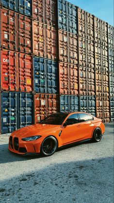 an orange sports car parked in front of stacked shipping containers