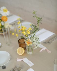 the table is set with yellow and white flowers in vases, napkins, and silverware