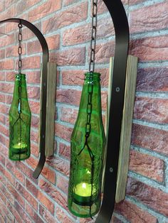 two green glass bottles are hanging from a metal hook on a brick wall with a chain attached to it