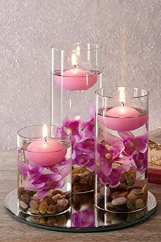 pink flowers and candles in glass vases on a tray with rocks, nuts and bread