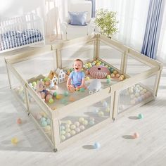 a baby sitting in a playpen with balls all around it and stuffed animals on the floor