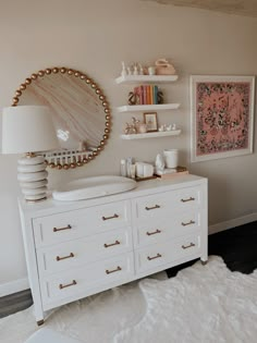 a white dresser sitting next to a wall with shelves on it and a mirror above it