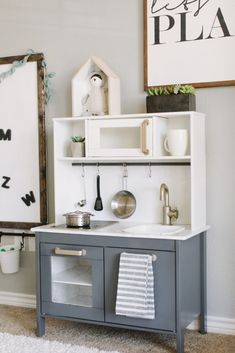 a gray and white play kitchen in a child's room with shelves above the sink