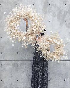 a woman is holding a wreath with flowers on it and standing in front of a concrete wall