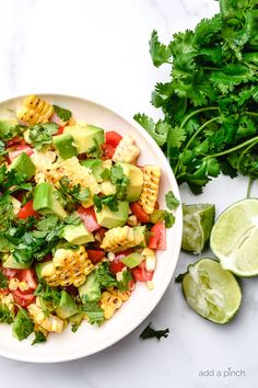 a white bowl filled with corn salad next to cilantro and lime wedges