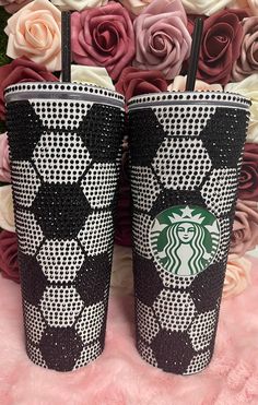 two starbucks cups with black and white designs on them sitting next to pink rose flowers