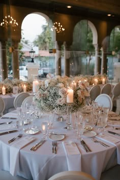 the table is set with white flowers and candles for an elegant wedding reception or special event