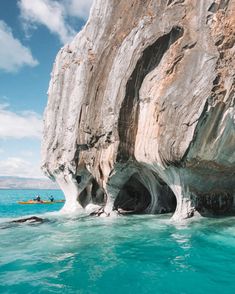 two kayakers are in the blue water near a large rock formation that has been carved into it's sides