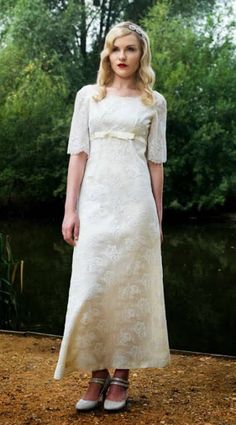 a woman in a white dress standing next to a river and trees with her hands on her hips