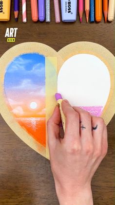 someone is drawing on a heart shaped paper with crayons