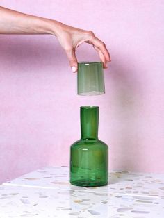 a green glass bottle with a hand reaching for it to touch the top one off