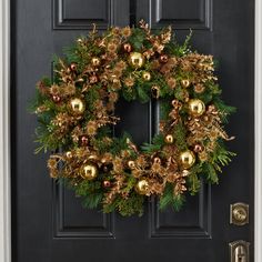 a christmas wreath with gold ornaments hanging on a black front door, surrounded by greenery and pine cones