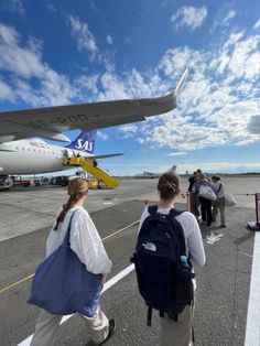 two people are walking towards an airplane on the tarmac with luggage and backpacks