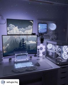 two computer monitors sitting on top of a desk in front of a wall with snow covered mountains