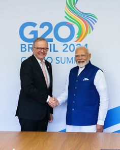 two men shaking hands in front of the g20 summit sign and logo behind them