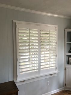 an empty room with white shutters in the window and wood flooring on the walls